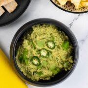 Coriander and green chilli houmous in a black serving bowl garnished with coriander leaves and sliced green chillis.