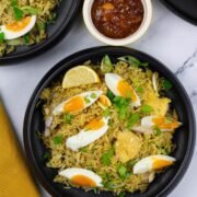 Two portions of kedgeree in black bowls with a small dish of mango chutney on the side.