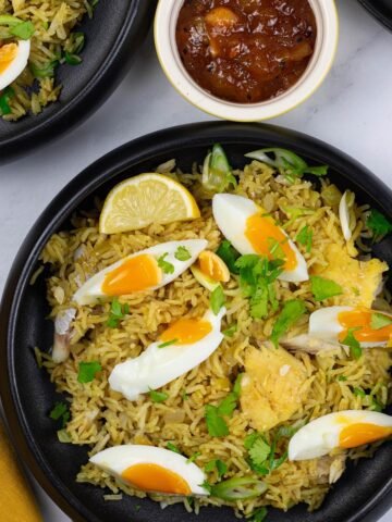 Two portions of kedgeree in black bowls with a small dish of mango chutney on the side.