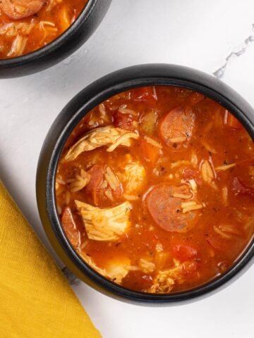 Two portions of Spanish chicken, chorizo and rice soup in black bowls.