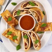 Sliced stromboli on an oval white platter, garnished with basil leaves and served with a dish of tomato pizza sauce.