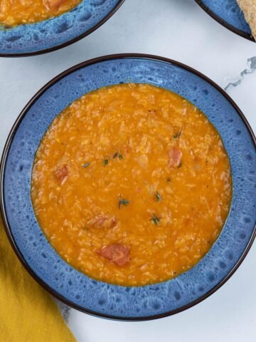 Two portions of tomato, lentil and thyme soup, made in the Thermomix, in blue patterned bowls with a plate of sliced brown bread on the side.