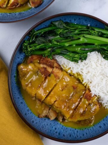 Two portions of Wagamama chicken katsu curry in blue patterned bowls with basmati rice and tenderstem broccoli.