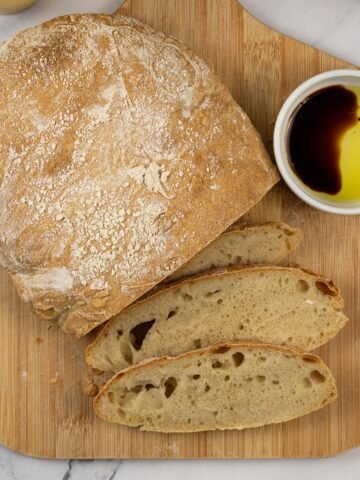 Ciabatta bread on a board with 3 pieces sliced and a small dish of extra virgin olive oil and balsamic vinegar.