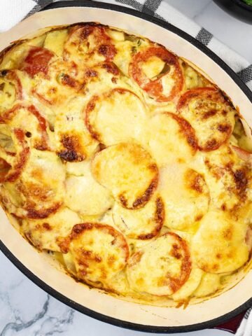 Creamy gratin of smoked haddock, tomatoes and potatoes in a deep oval casserole dish.