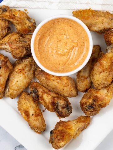 Easy air fryer cajun chicken wings on a white square platter with a dish of cajun dipping sauce and paper napkins on the side.