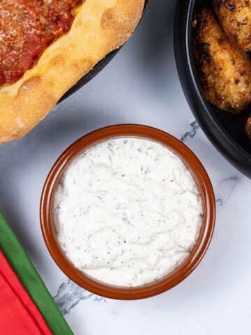 Garlic and herb dip in a small round terracotta dish with a Chicago deep pan pizza and easy air fryer Spanish chicken wings on the side.