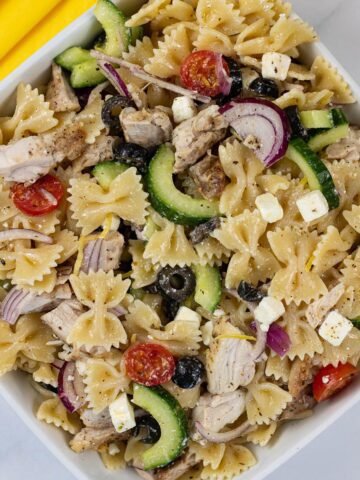 Greek chicken pasta salad in a square white serving dish with yellow napkins on the side.