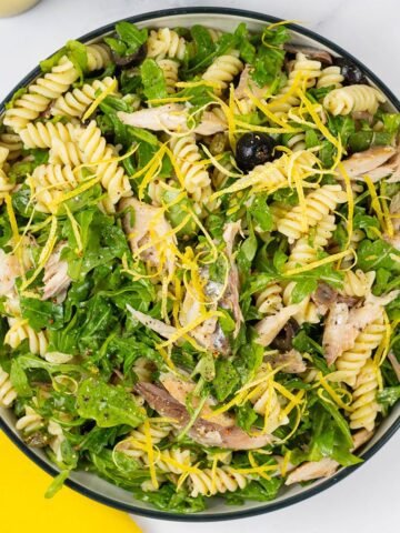 Hot smoked mackerel and rocket pasta salad in a black and cream serving bowl.