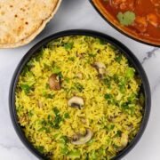 Mushroom rice in a black serving bowl with a plate of chapatis and dish of speedy gunpowder chicken in the background.
