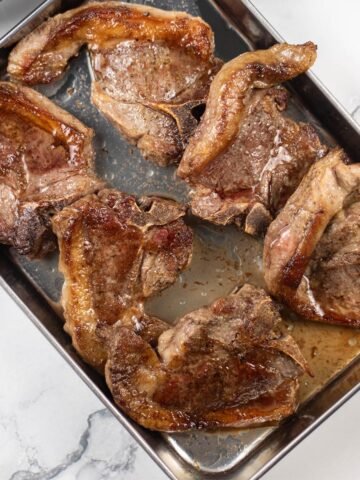 6 perfect pan-fried lamb chops resting on a tray.