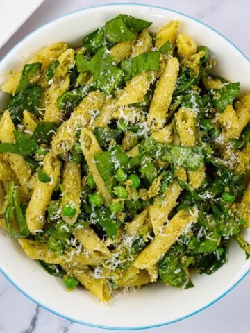 Pesto, peas and spinach pasta salad in a light blue trimmed serving bowl.