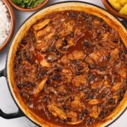 Pulled chicken and black bean chilli in a large round shallow casserole dish with dishes of rice, coriander and tortilla crisps on the side.