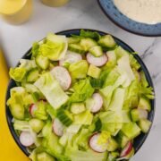 Simple crunchy lettuce salad in a blue serving bowl with a small bowl of ranch dressing and yellow salt and pepper grinders in the background.