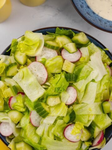 Simple crunchy lettuce salad in a blue serving bowl with a small bowl of ranch dressing and yellow salt and pepper grinders in the background.