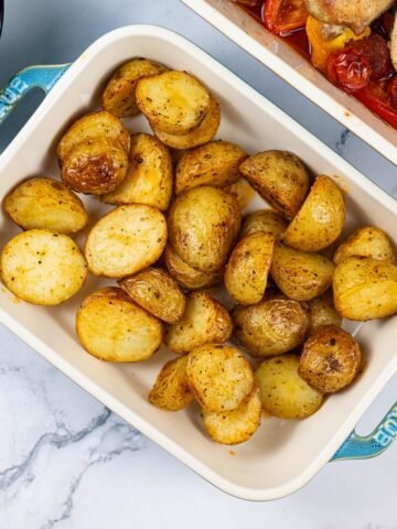 Spanish-style roast baby potatoes in a small rectangle Staub oven dish, with a large dish of Spanish chicken traybake in the background.