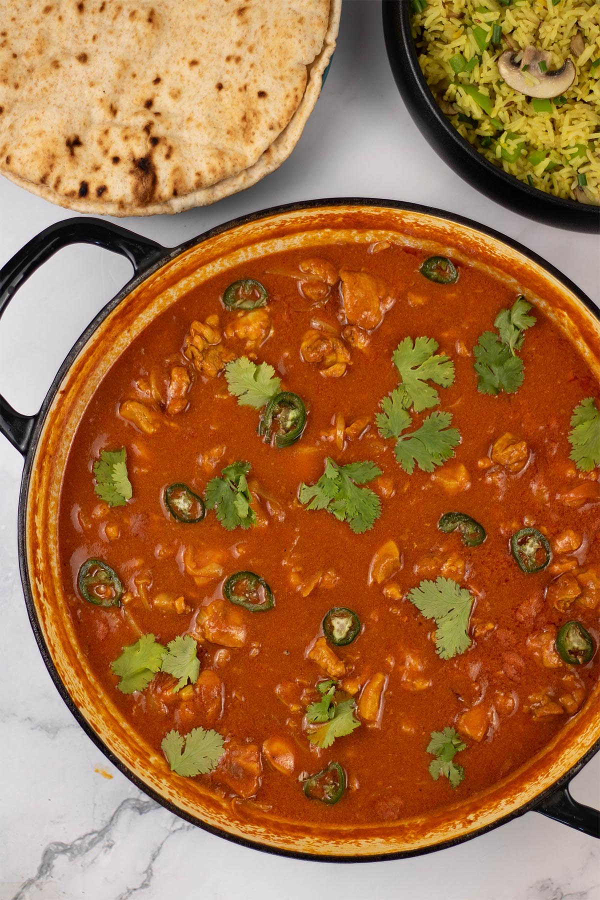 Speedy gunpowder chicken in a large shallow casserole dish with a plate of chapatis and bowl of mushroom rice in the background.