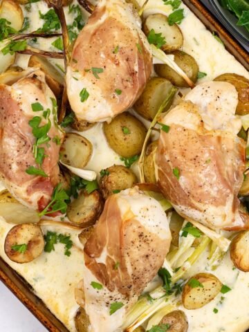 Four portions of parma ham, chicken and creamy potato traybake on a large baking tray, with a bowl of spring greens the side.