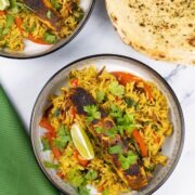 2 portions of Balti salmon rice bowls in black and white bowls with a wedge of lime and plate of garlic bread on the side.