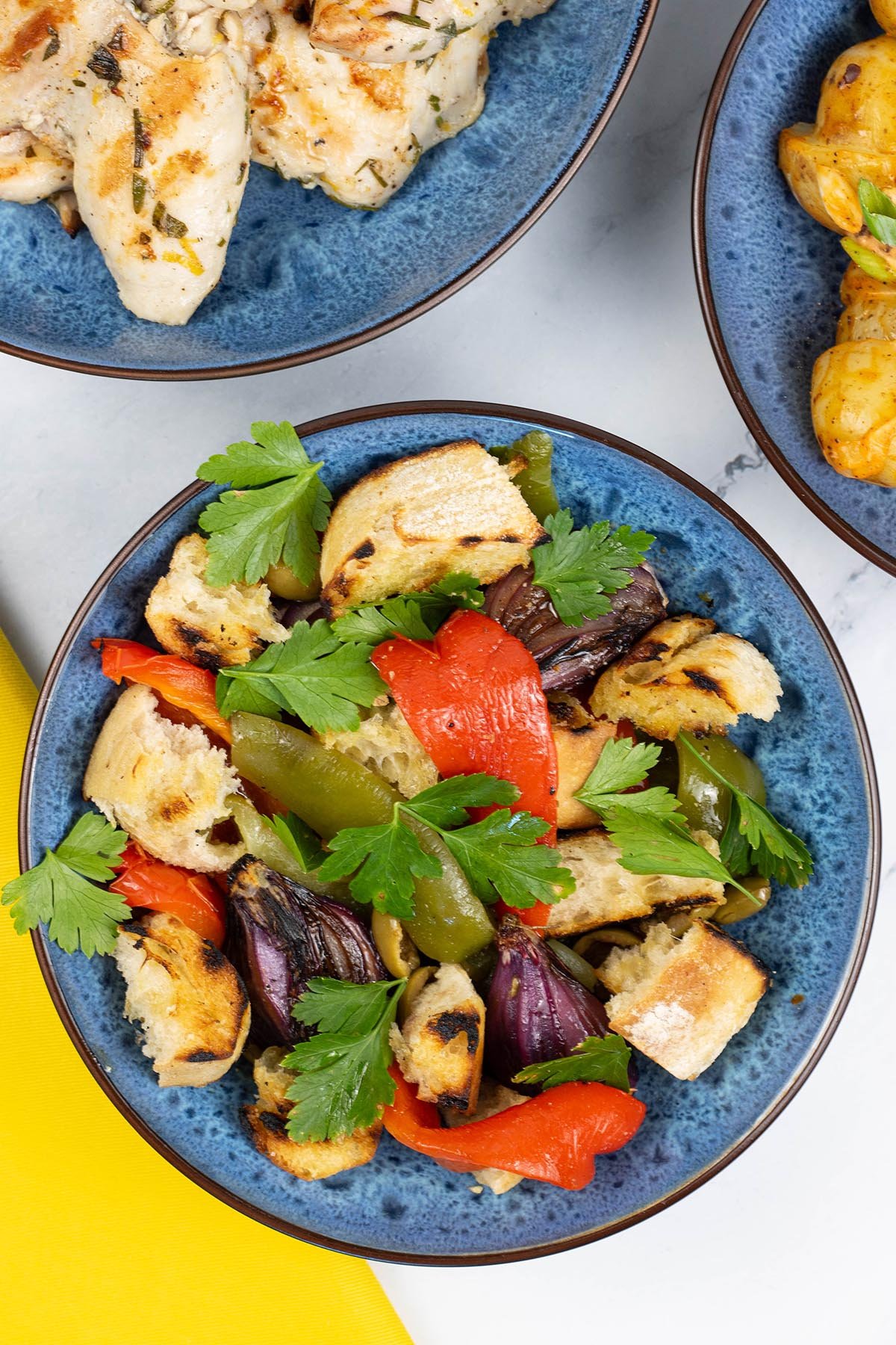 Barbecued mixed pepper salad for 2 in a blue patterned bowl with a dish of lemon herb chicken thighs on the side.