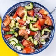 Greek salad in a blue and white striped bowl with a yellow napkin on the side.