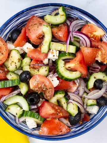 Greek salad in a blue and white striped bowl with a yellow napkin on the side.