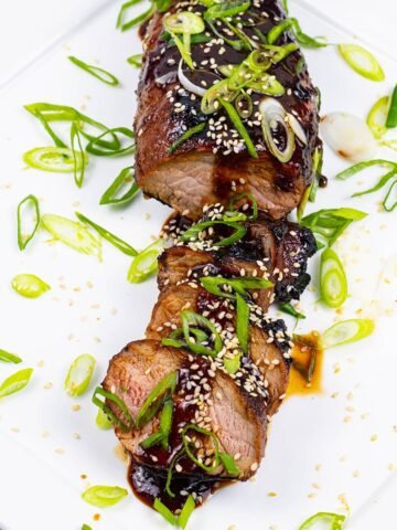 Korean barbecued pork fillet sliced and garnished with spring onions on a square white platter.