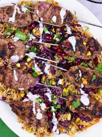 Lamb koftas with jewelled rice on an oval white platter with a green napkin on the side.