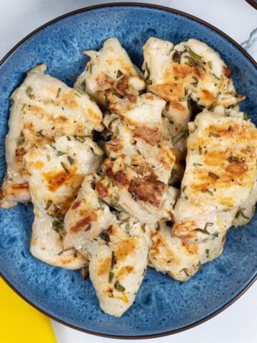 Lemon herb chicken thighs in a blue patterned serving bowl with a yellow napkin on the side.