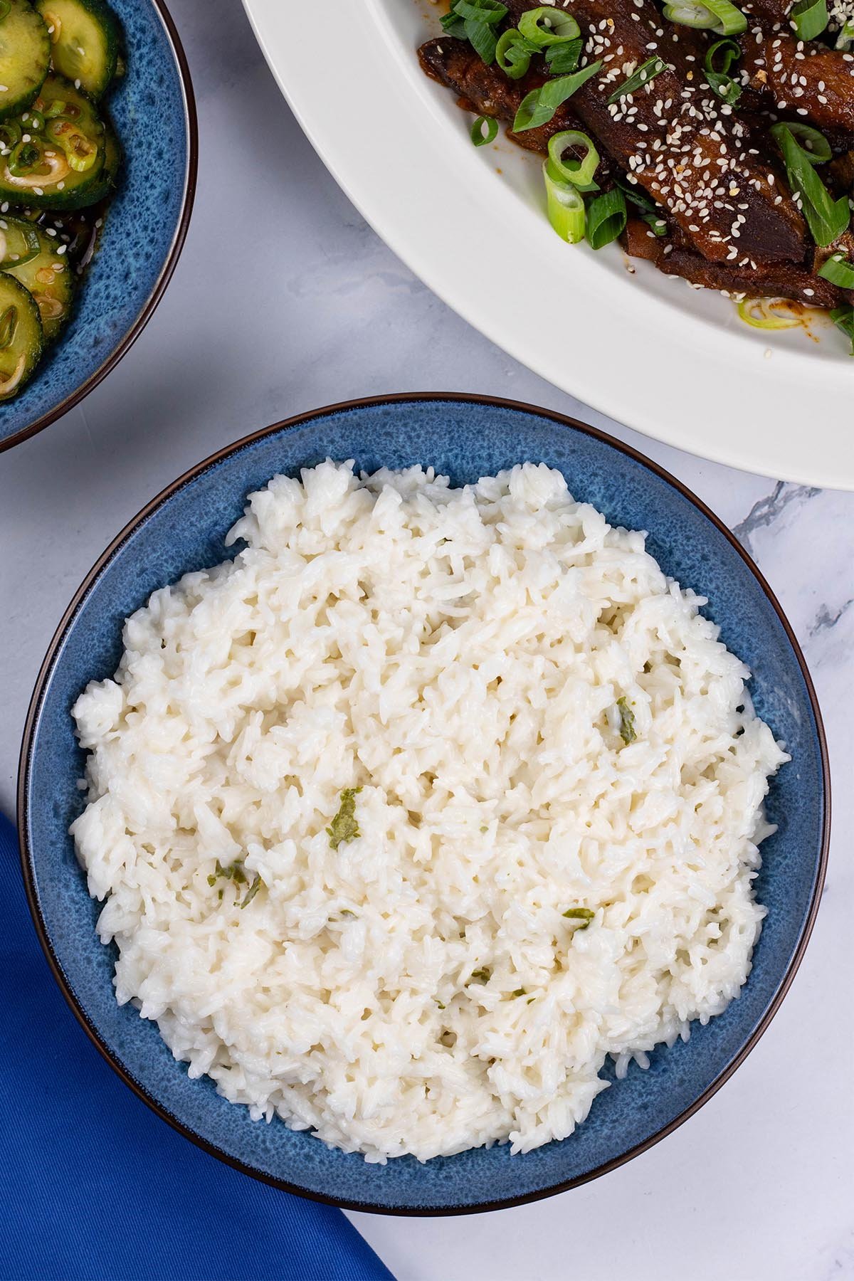 Coconut rice in a blue patterned serving bowl with a platter of slow cooker gochujang pork ribs in the background.