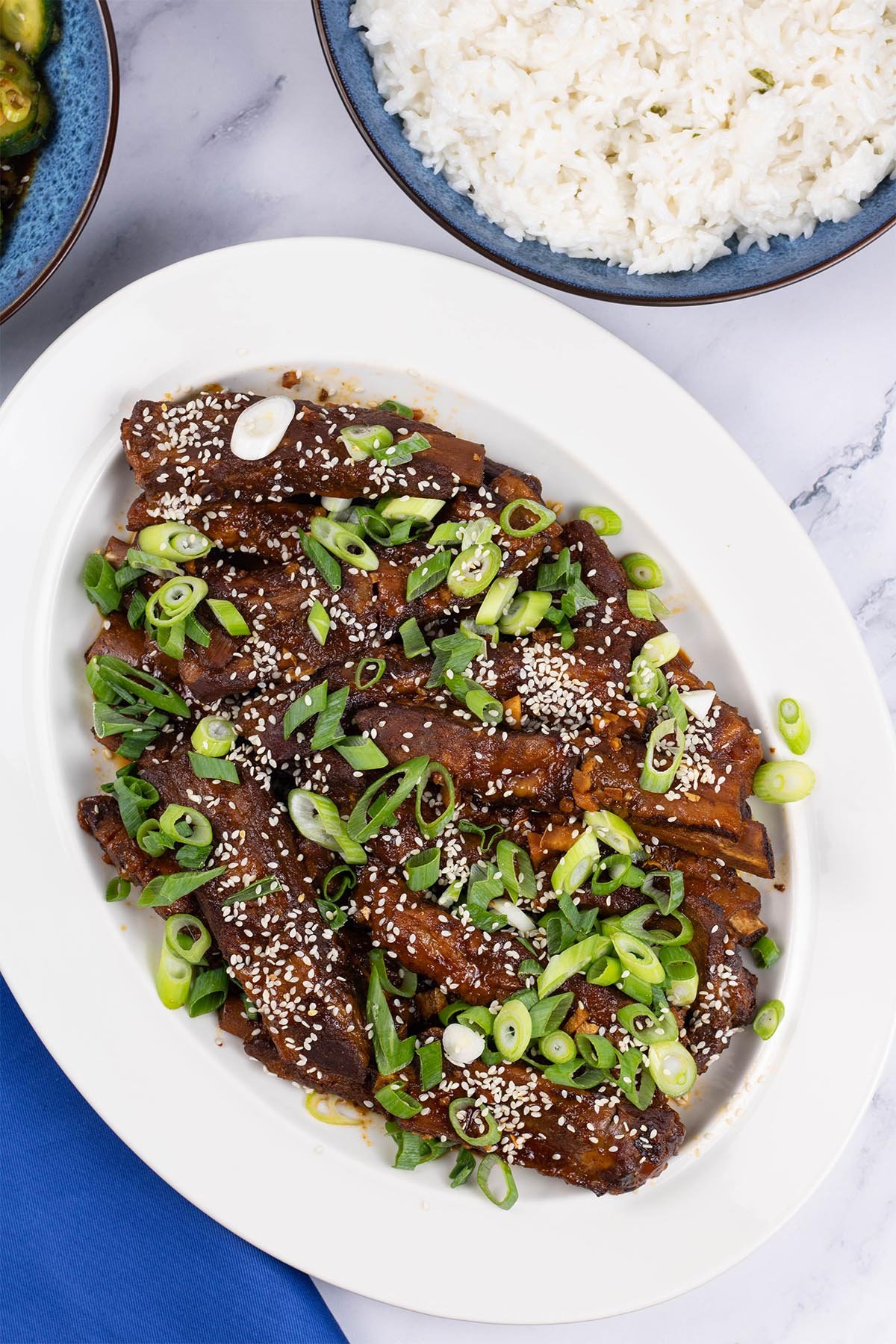 Slow cooker gochujang pork ribs on an oval white platter with a bowl of coconut rice in the background.