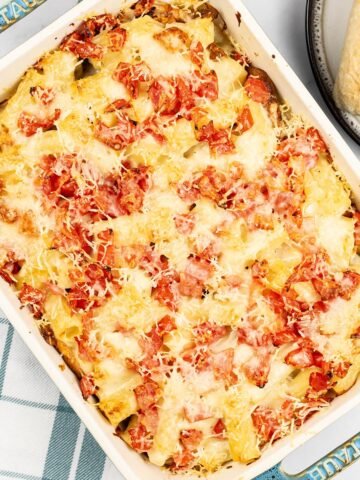 Chicken pasta bake in a rectangle Staub ovenproof dish with a teal and white checked towel on the side.