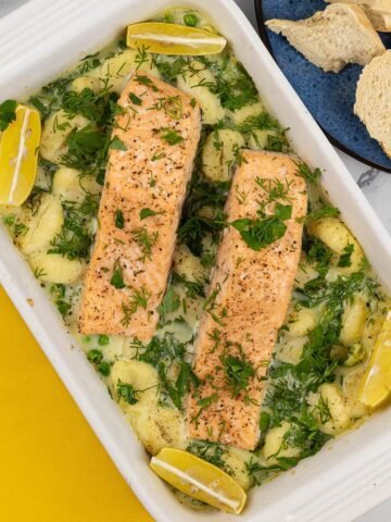 Two portions of salmon with gnocchi, peas and broad beans in a white rectangle oven dish.