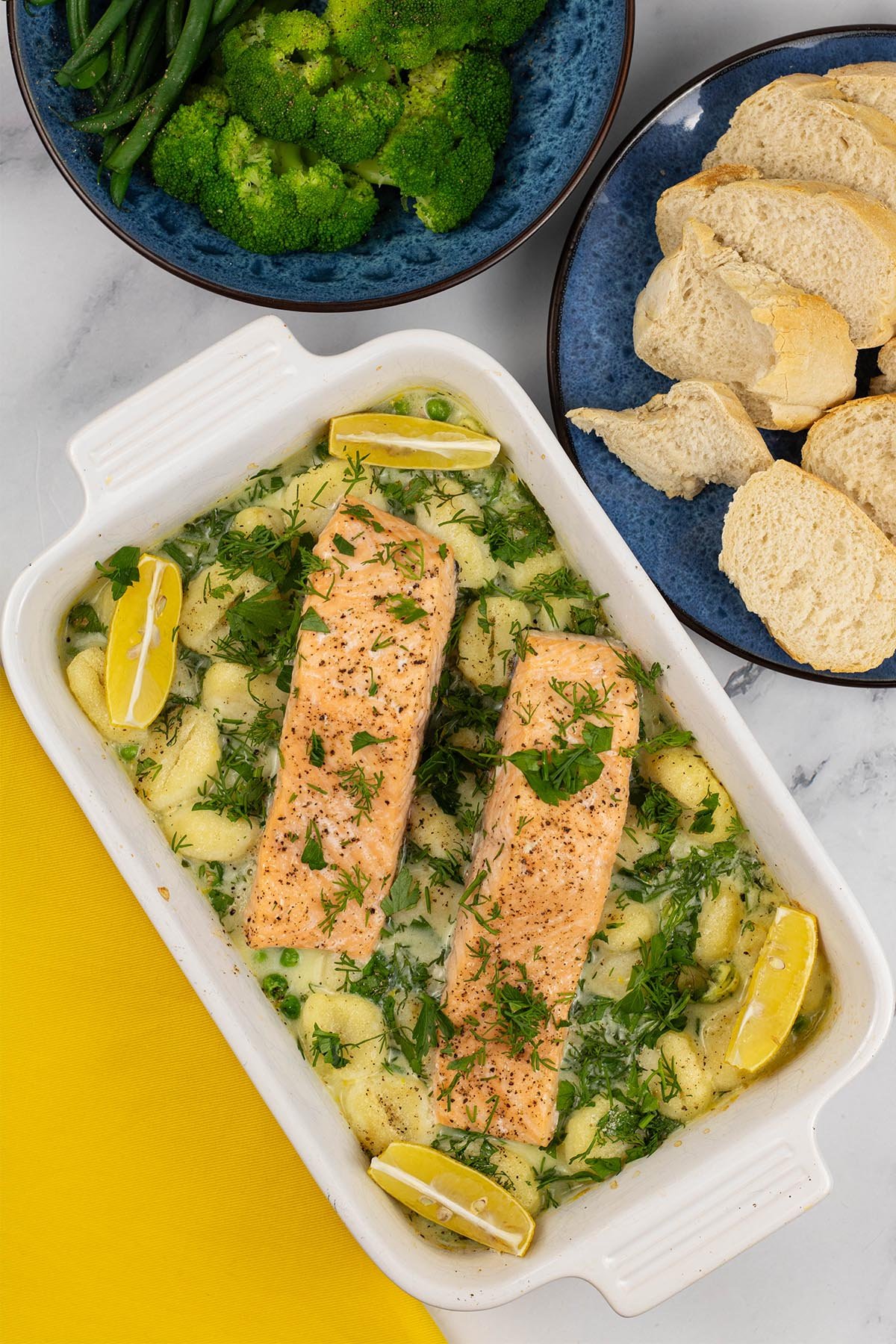 Two portions of salmon with gnocchi, peas and broad beans in a white rectangle oven dish.
