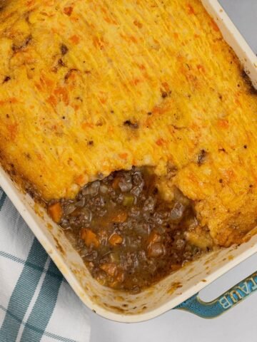 Venison mince pie in a rectangular Staub ovenproof dish with a checked teal and white towel on the side.