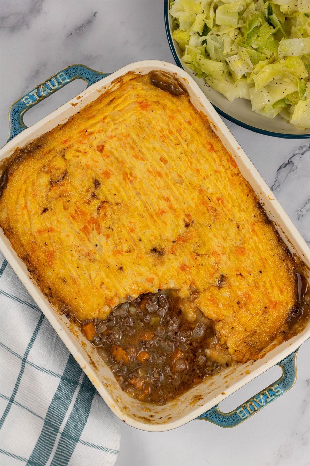 Venison mince pie in a rectangular Staub ovenproof dish with a bowl of easy buttered cabbage on the side.
