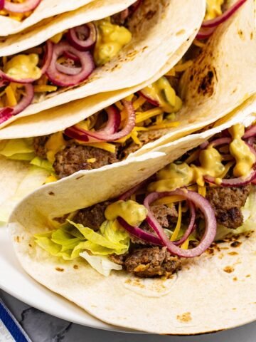 4 cheeseburger tacos on a white oval platter with paper napkins on the side.