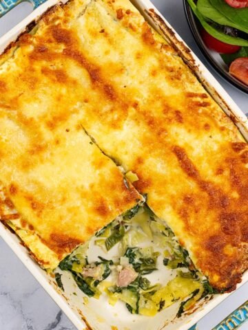 Ham, spinach and mozzarella lasagne in a rectangle Staub oven dish with a portion removed and a bowl of salad on the side.