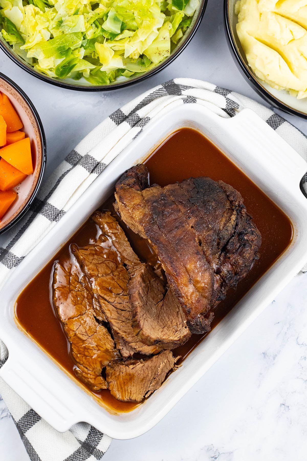 Slow cooker beef pot roast sitting in a white rectangular serving dish with gravy and a couple of slices carved.