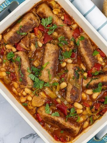 Slow cooker sausage casserole in a rectangle Staub serving dish with a baguette in the background.
