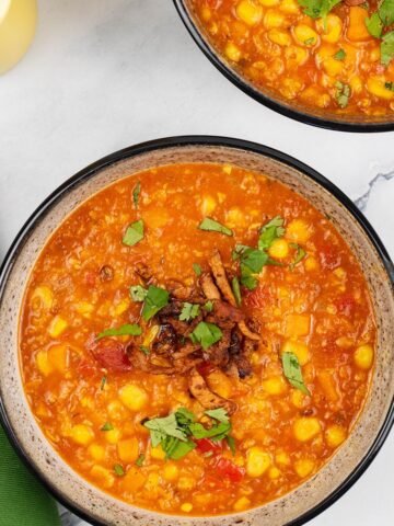 Two portions of spicy sweetcorn soup in black patterned bowls with yellow salt and pepper grinders and a green napkin on the side.