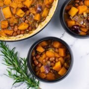 Two portions of sumptuous squash soup in black bowls with a sprig of rosemary on the side.