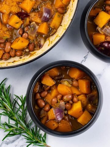 Two portions of sumptuous squash soup in black bowls with a sprig of rosemary on the side.